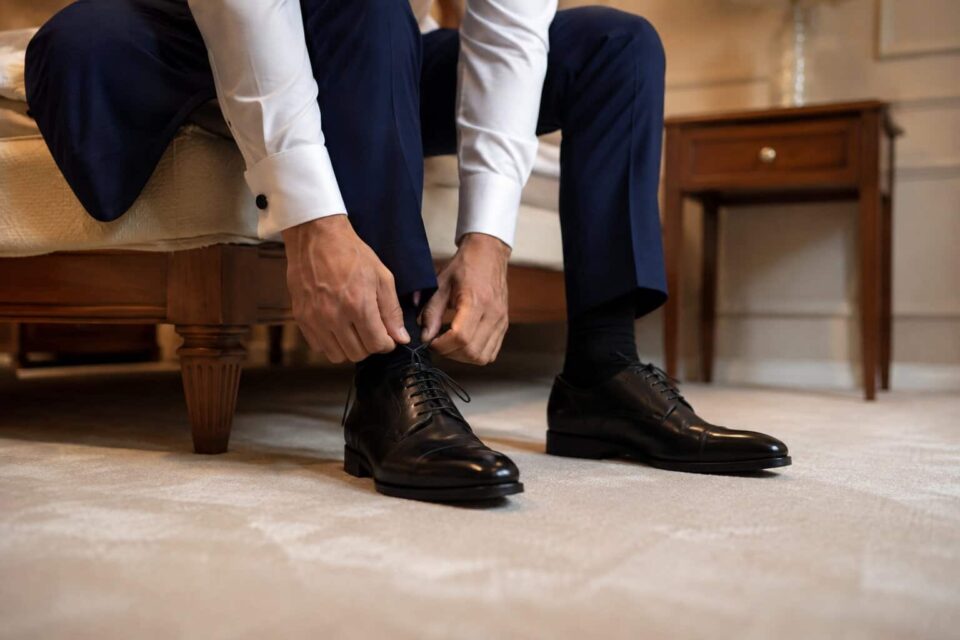 Un marié ajustant ses souliers noirs élégants pour savoir comment porter des chaussures de mariage neuves sans douleur.